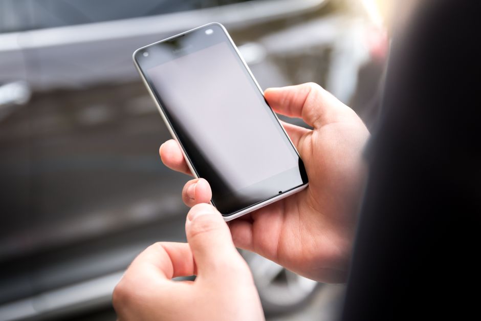 Close-up of hands holding a smartphone outdoors during the day.