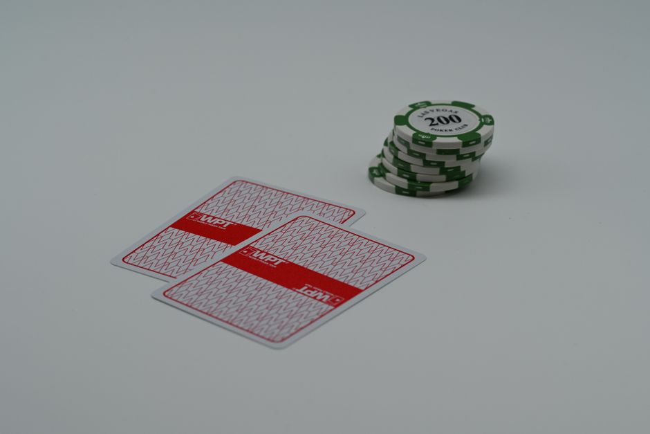 Close-up of poker playing cards and green chips on a white background, highlighting the simplicity of a gaming scene.